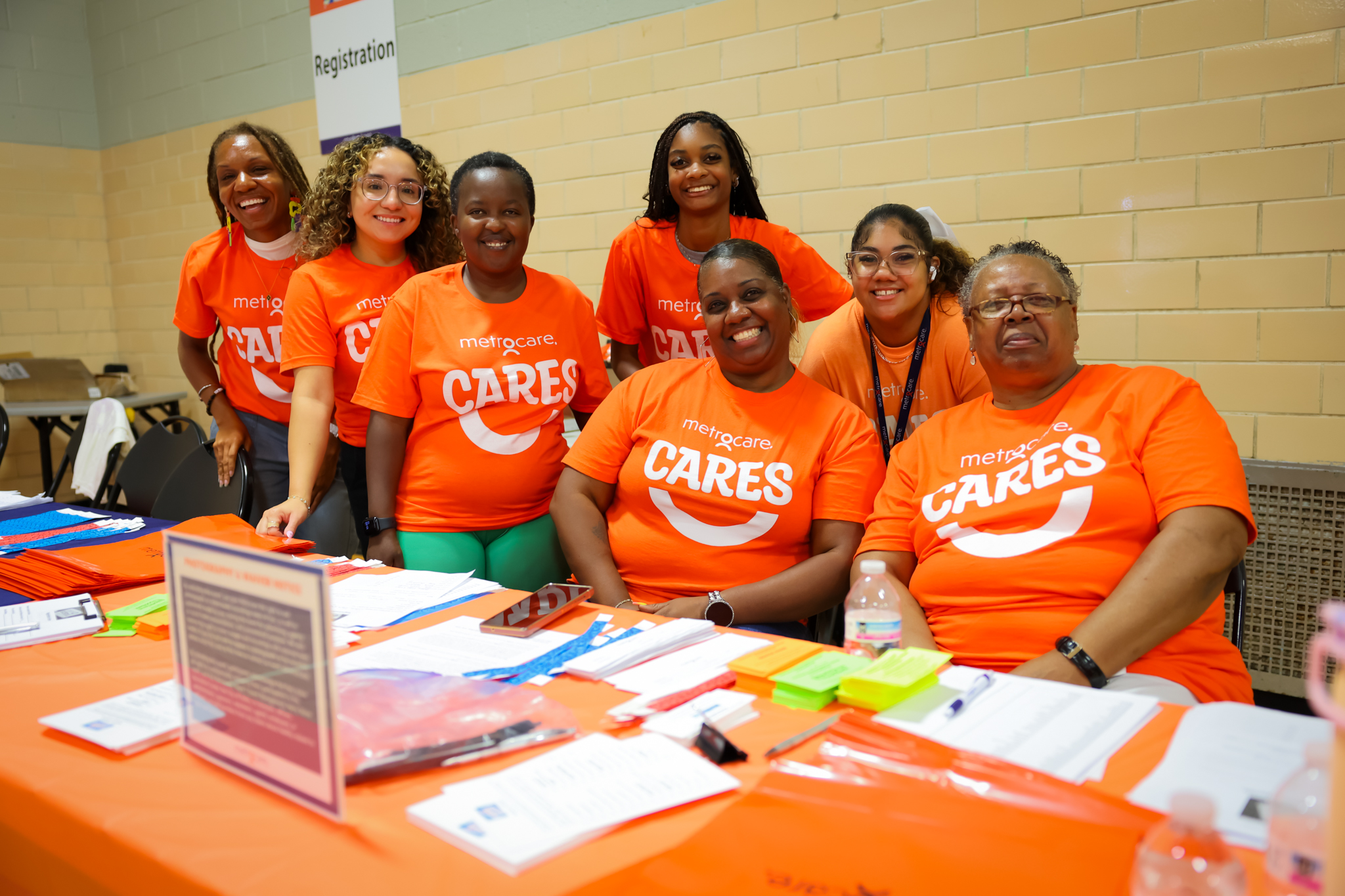 Art-874 Group of people wearing orange metrocare cares shirt at registration table smiling