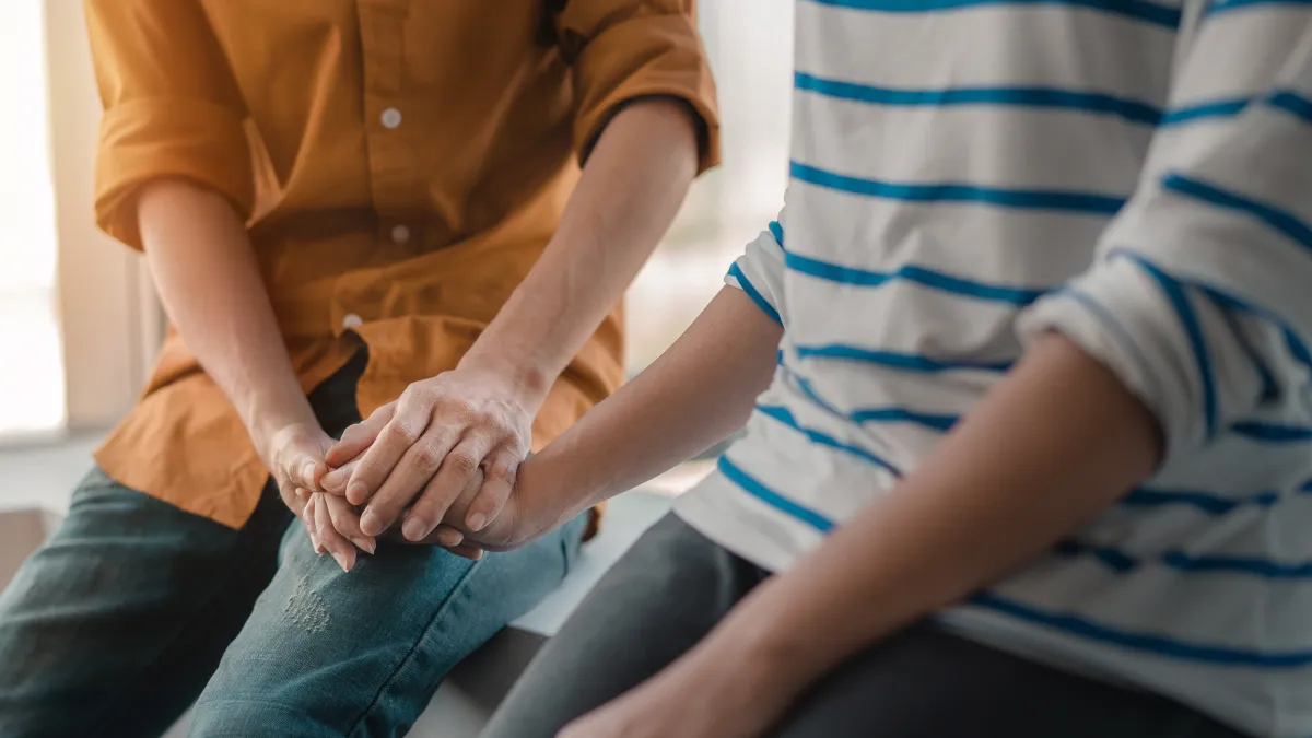 In The News 3 Two people seated side by side, with one person gently holding the other person’s hand.